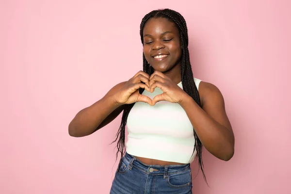 Cute woman making heart symbol. Young female model in turquoise T-shirt showing heart with hands smiling. Portrait, studio shot, support concept