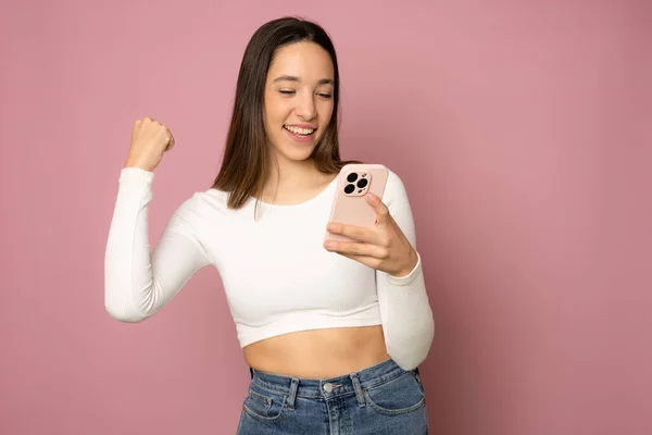 Jonge Vrouw Geïsoleerde Roze Achtergrond Met Telefoon Overwinningspositie — Stockfoto