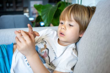 Kanepede oturmuş parmaklarına bakan küçük şirin bir çocuğun portresi.