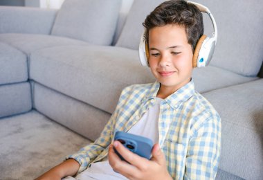 Ekose gömlekli çocuk evdeki kanepede akıllı telefon kullanıyor.