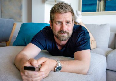 Hafta sonu eğlence aktiviteleri. Milenyum Kafkasyalı uzaktan kumandalı televizyondaki kanalları değiştiren adam. Mutlu genç adam TV 'de ilginç bir program izliyor.