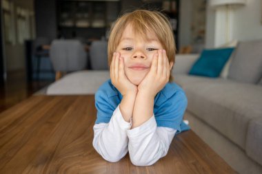 Oturma odasındaki masada uzanmış gülümseyen çocuğun yakın çekimi.