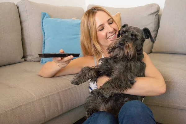 Young smiling woman with cute schnauzer dog watching TV at home