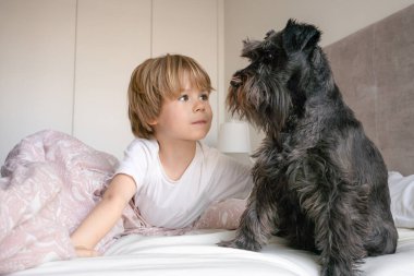 Sevimli sarışın çocuk, yeni yürümeye başlayan çocuk, evcil köpeğiyle yatakta yatıyor.