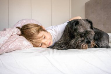 Sevimli sarışın çocuk, yeni yürümeye başlayan çocuk, evcil köpeğiyle yatakta yatıyor.