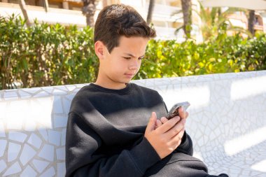 12 yaşında bir çocuk açık havada akıllı telefon kullanıyor..