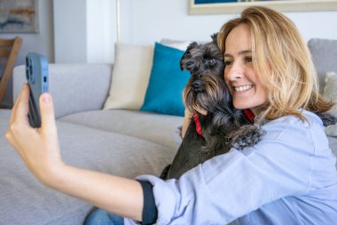 Genç ve güzel bir kadın evde tatlı köpeğiyle harika vakit geçiriyor. Bir sürü fotoğraf çekiyor. Yaşam tarzı ve arkadaşlık kavramı.