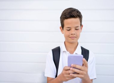 Beyaz arka planda tek başına duran çocuk akıllı telefonunu kullanıyor. Gençlerin sosyal konseptleri: Çevrimiçi zorbalık, arkadaş baskısı, sosyal medya rekabeti, sosyal ağ oluşturma