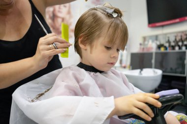 Yumuşak odaklı küçük çocuk berber dükkanında budanır. Yüzünde parlak duygular, yüz ifadesi, saç kesme süreci..