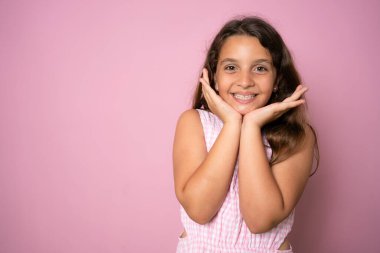 Gülümseyen kahverengi saçlı bir kızın portre resmini yakın plan çek. Pembe arka planda mutlu ve güzel bir çocuk, on yaşında bir çocuk kameraya bakıyor ve poz veriyor.