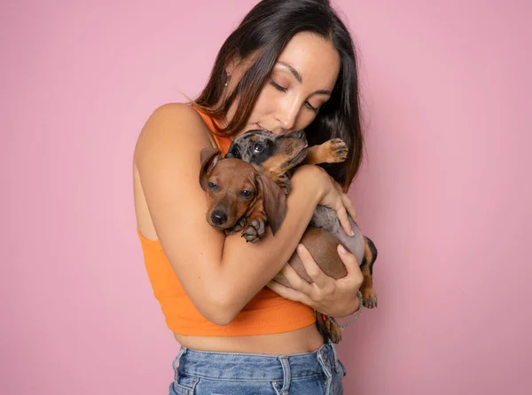 可爱的黑发女人抱着和拥抱着与粉红背景隔离的腊肠狗 爱动物 宠物的概念 抱着Dachshund小狗的快乐女人 — 图库照片