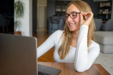 Bilgisayarla çalışan güzel genç bir kadın konsantre olmuş ve gülümsüyor.