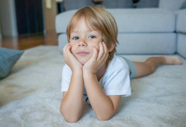 Evdeki halıya uzanmış gülümseyen küçük bir çocuğun portresi.