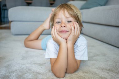 Evdeki halıya uzanmış gülümseyen küçük bir çocuğun portresi.