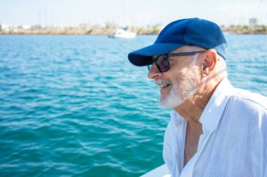 Deniz tatilinin ya da emekliliğin tadını çıkarırken gülümseyen yaşlı bir adamın portresi. Bulutlu gökyüzü ve ufukta su.