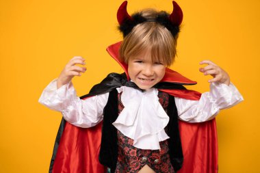 Cadılar bayramında vampir gibi giyinen küçük çocuk turuncu arka planda izole edilmiş..