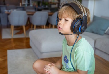 Kulaklıklı küçük çocuk oturma odasında video oyunu oynuyor.