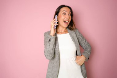 Gülümseyen genç bir iş kadınının portresi cep telefonuyla konuşuyor ve pembe arka planda izole edilmiş fotokopi alanına bakıyor.