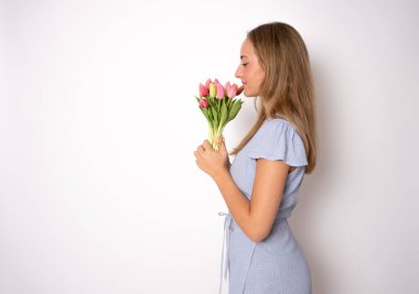 Beyaz arka planda izole edilmiş pembe çiçekleri elinde tutan güzel, neşeli kızın portresi.