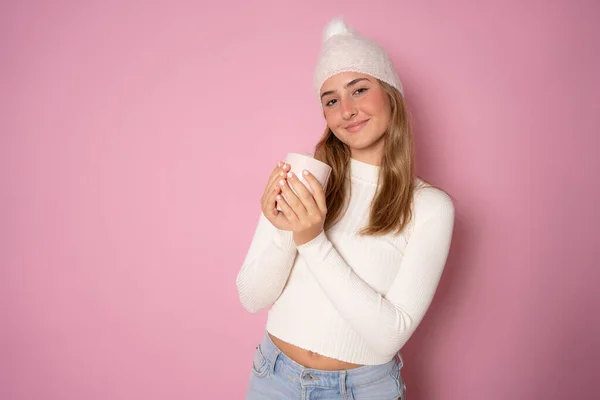 快乐的年轻女子戴着冬帽 孤零零地站在粉红的背景下 举着一杯 — 图库照片