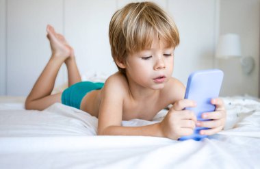 Beyaz çocuk yatak odasında yatarken akıllı telefon kullanıyor.
