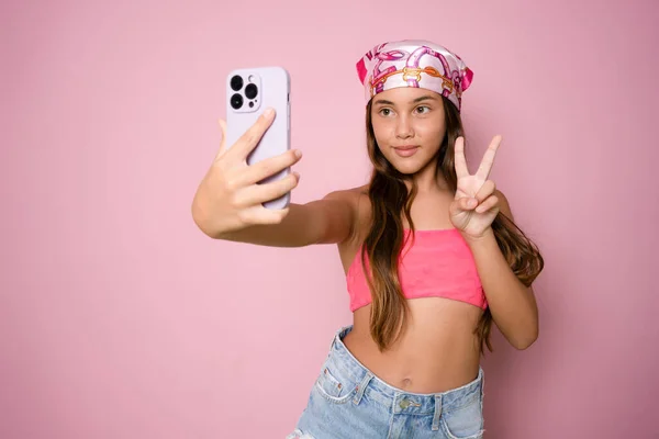 Uzun esmer saçlı, pembe arka planda akıllı telefonu izole ederek gülümseyen küçük Latin bir kızın fotoğrafı.