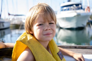 Mutlu çocuk can yeleği giyer ve temiz havanın tadını çıkarırken gemi güvertesinde yüzen deniz suyunda metal çitlere bakar durur.