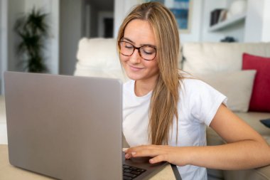 Kanepede oturan ve evinde dizüstü bilgisayar kullanan genç bir kadın ressamın portresi.