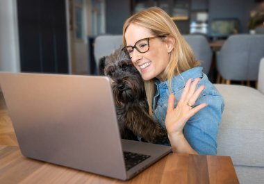 Neşeli kadın dizüstü bilgisayar kullanıyor köpekle masada oturuyor uzaktan çalışıyor.