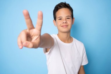 Kafkasyalı genç çocuk barış sembolü yapıyor. Yüzünde parmaklar, gülümseyerek zaferi gösteriyor.