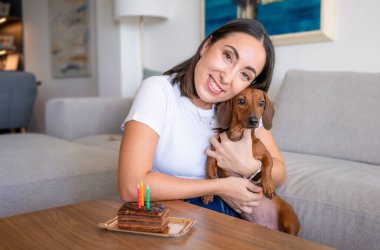 Güzel, neşeli genç bir kadın evcil köpeğinin doğum gününü evde kutluyor.