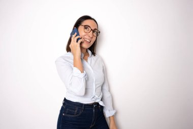 Gözlük ayakta neşeli çekici genç iş kadını ayakta ve beyaz arka plan üzerinde cep telefonu kullanarak