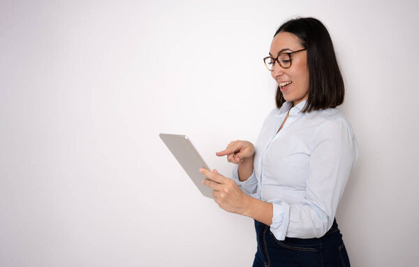 Image of young woman holding tablet and smiling, standing over white background