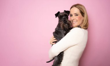 Cute young woman hugs her puppy schnauzer dog. Love between owner and dog. Isolated on pink background. Studio portrait.