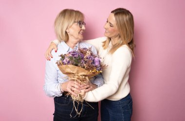 Moda, çekici, neşeli anne ve kız birlikte tatilin tadını çıkarıyorlar. Büyük, kusursuz, renkli lale buketleri, pembe arka planda izole edilmiş keyifli eğlence konsepti.