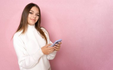 Pembe arka planda izole edilmiş akıllı bir telefonu kullanan ve okuyan güzel bir kadın.