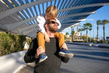 Baba ve oğlu güneşli parkta. Dışarıda oynayan sevgi dolu bir aile. Babası küçük çocuğu havada tutuyor. Genç adam ve onun sevimli küçük oğlu oynuyorlar ve gülüyorlar. Mutluluk ve sevgi. Babalar günün kutlu olsun..