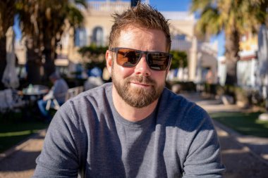 Güneşli bir günde güneş gözlüğü takan yakışıklı sakallı genç bir adam.