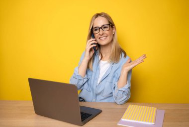 Akıllı telefondan konuşan genç iş kadını sarı arka plan üzerinde çalışıyor..