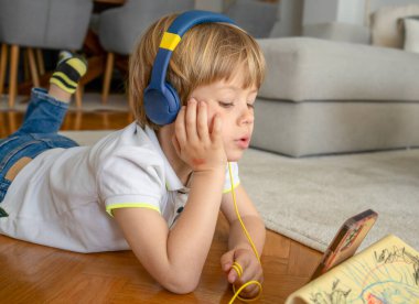 Halıya uzanmış, kulaklık takmış ve akıllı telefon kullanan bir çocuk.