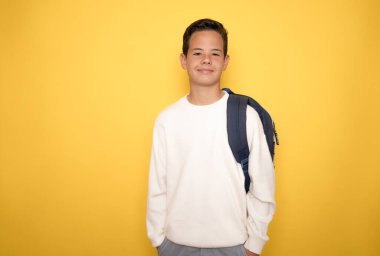 Gülümseyen küçük çocuk, sarı arka planda izole bir şekilde okulda kitap okumak için günlük kıyafetlerle fotokopi alanını işaret ediyor.