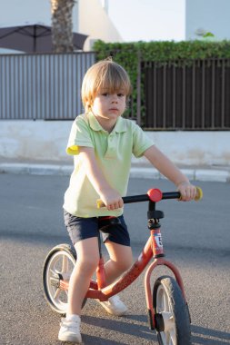 Küçük sevimli beyaz çocuk şehir parkındaki yolda bisiklet sürerken eğleniyor..