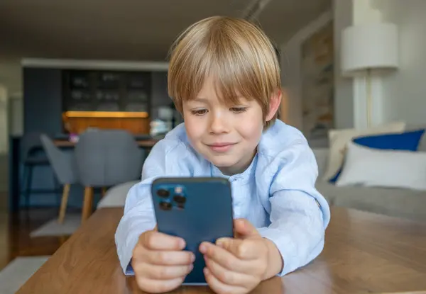 Evdeki masada akıllı telefon kullanan sevimli beyaz bir çocuğun portresi.