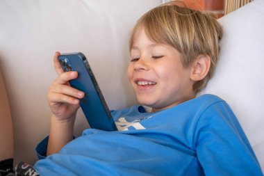 Odada kanepede akıllı telefon olan küçük çocuk. İnternet tehlikesi