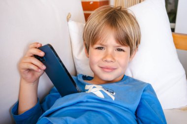 Odada kanepede akıllı telefon olan küçük çocuk. İnternet tehlikesi