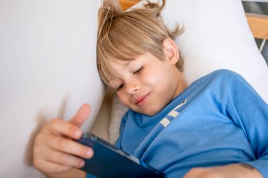 Evdeki kanepede uzanmış akıllı telefon kullanan sevimli beyaz çocuk.