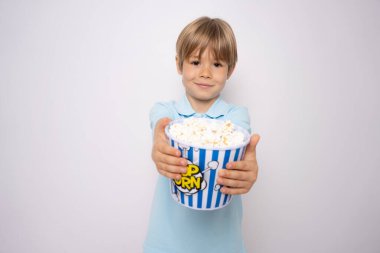 Beyaz arka planda izole edilmiş küçük beyaz çocuk elinde koca bir kova patlamış mısır tutuyor.