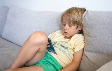 Çocuk evdeki oturma odasındaki koltukta akıllı telefon kullanıyor..