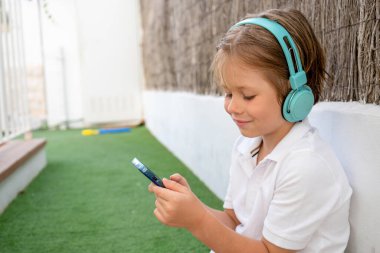 Parkta akıllı telefon kullanarak kulaklık takan gülümseyen çocuk..