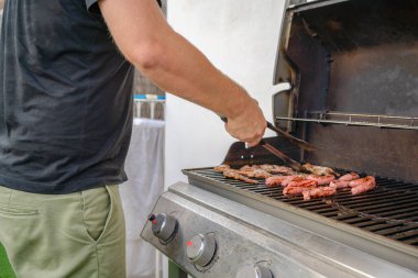 Güneşli yaz gününde bahçede barbekü yapan bir adam.